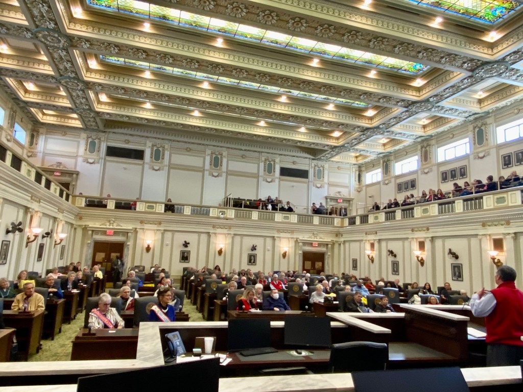 People sitting in the House chamber seats listening to a speaker